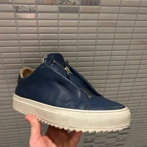 Blåa Axel Arigato zip - Ett riktigt bra erbjudande, med tanke på att denna modell inte längre säljs. Vid hälen på insidan av skorna finns det lite slitage, men detta syns inte från utsidan. Annars är de i bra skick. OBS priset kan diskuteras.