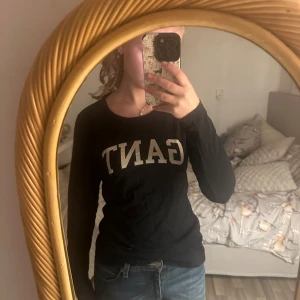 Svart långärmad tröja från GANT - Snygg svart långärmad tröja från GANT med logga framtill. Perfekt för en stilren och avslappnad look. Passar bra till jeans eller kjol.