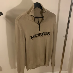 Beige tröja från Morris - Tja Säljer en stilren beige tröja från Morris Sporting Club med dragkedja och hög krage. Tröjan har långa ärmar och ett broderat logotyp på framsidan. Perfekt för en avslappnad och snygg look.