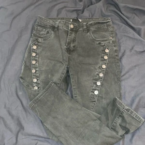 Gröna jeans med knapprad - Snygga gröna jeans med unik knapprad längs benen. De har en klassisk femficksdesign och en bekväm passform. Perfekta för en cool och avslappnad stil.