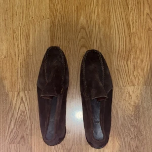 Bruna mockaloafers från Lacoste - Snygga bruna loafers i mocka från Lacoste. Perfekta för en stilren look med en bekväm passform. Diskret design med märkets logga på hälen.