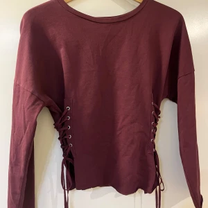Vinröd tröja med snörning - En snygg vinröd tröja med långa ärmar och snörning på sidorna. 