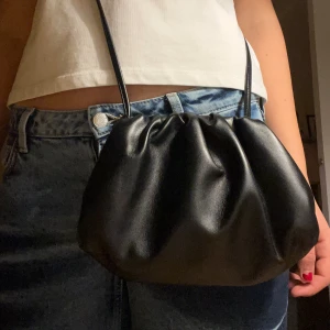 Svart clutch väska - Nypris 599kr!! Snygg svart axelväska i syntetmaterial med en enkel och stilren design. Väskan har en praktisk storlek och en smal axelrem som gör den lätt att bära. Mycket får plats i och är i ny skick, aldrig använd!