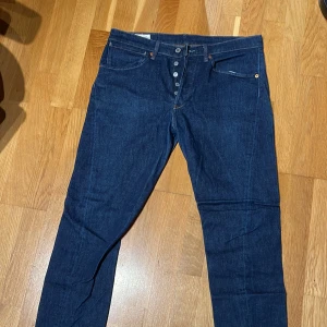 Levi's 512 jeans - Snygga Levi's 512 jeans i mörkblå denim med klassisk femficksdesign och knappgylf. Perfekta för en stilren look.