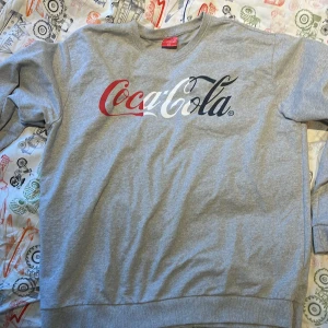 Grå sweatshirt med Coca-Cola-tryck - Hej! Jag säljer min Coca-Cola tröja. Den är knappt använd men jag har haft på mig den max 4 gånger. Snälla ge ett bud!
