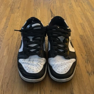 Nike Dunk i svart och vitt - Säljer ett par klassiska Nike Dunk sneakers i svart och vitt. Skorna har en stilren design med snörning och en bekväm passform. Perfekta för en avslappnad stil. Skorna är använda mycket och har en del defekter. 