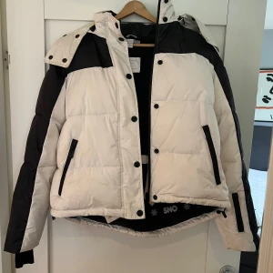 Vit och svart jacka med huva - Vinterjacka/Skidjackaz Svart och vit med huva som har svart fuskpäls i kanten. Köpt för ca 2000kr. Bara använd en semester dvs bra skick! Säljes för 500kr 