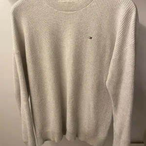 Vit stickad tröja från Tommy Hilfiger - Säljer en stilren vit stickad tröja från Tommy Hilfiger med ett diskret logotypbroderi på bröstet. Tröjan har en rund halsringning och långa ärmar, perfekt för kyligare dagar. Klassisk och tidlös design som passar till det mesta.