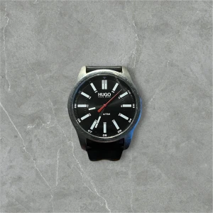 Svart klocka från Hugo - Snygg klocka från Hugo med svart urtavla. Den har en stilren design med tydliga markeringar och en svart rem. Perfekt för att ge en elegant touch till din stil.