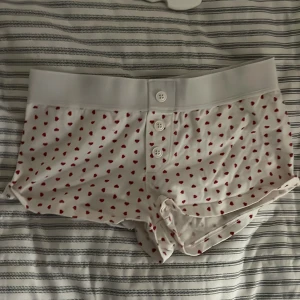 Vita shorts med hjärtmönster - Söta vita shorts med röda hjärtan och knappar framtill. Perfekta för en avslappnad dag hemma eller som pyjamasshorts.