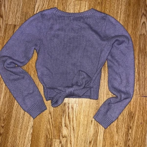 Lila stickad tröja från Hollister - Säljer en snygg lila stickad tröja från Hollister. Tröjan har långa ärmar och en knytning i midjan som ger en cool look. Perfekt för kyligare dagar!