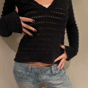 Svart ribbad tröja - Snygg svart ribbad tröja med v-ringning och långa ärmar. Perfekt för en trendig look med jeans. Tröjan har en unik struktur med små hål som ger en cool detalj.