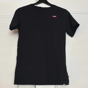 Svart t-shirt från Levi's - Snygg svart t-shirt från Levi's med klassisk passform. Den har en liten röd Levi's-logga på bröstet och är tillverkad i mjuk bomull. Perfekt för en stilren vardagslook.