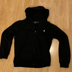 Ralph lauren zip hoodie - Säljer en stilren zip hoodie från ralph lauren. Perfekt för en avslappnad look. Hoodien har långa ärmar och en bekväm passform. Den är endast använd 2-3 gånger och i perfekt skick. Hör av er om ni undrar något.