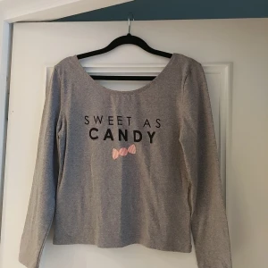 Grå tröja med texten 'Sweet as Candy' från H&M  - Säljer en grå långärmad tröja med texten 'Sweet as Candy' och en söt rosa rosett på framsidan. Perfekt för en avslappnad stil.