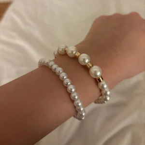 Pärlarmband och örhängen - Elegant set med pärlarmband och matchande örhängen. Armbandet har vita pärlor med gulddetaljer, medan örhängena är i en klassisk hoop-stil med vita pärlor. Perfekt för att ge en sofistikerad touch till din outfit.