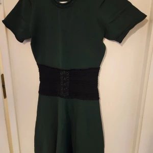 Grön klänning från Sandro Paris - Elegant grön klänning från Sandro Paris med korta ärmar och en markerad midja med snörning. Perfekt för en stilren look.