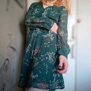 Blommig grön klänning - Snygg grön klänning med blommigt mönster. Den har långa ärmar och en v-ringad hals. Perfekt för en stilfull look.