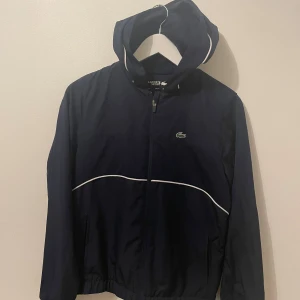 Lacoste jacka/Kofta - Lacoste zip kofta/jacka i marinblå storleken är 176cm men är liten i storleken den passar alltså 152-170cm