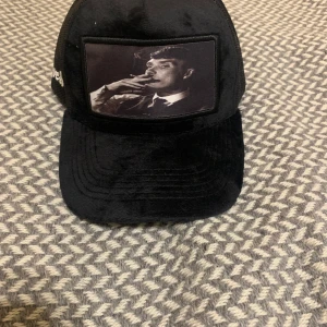 Svart och blå keps med motiv - Två kepsar från Averó med unika motiv. Den svarta kepsen har ett tryck av en person som röker, medan den blå kepsen har ett tryck av en sportbil. Båda kepsarna har mesh på sidorna och broderad logotyp.