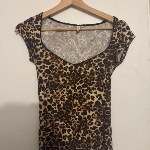 Leopardmönstrad topp från Nelly - Snygg leopardmönstrad topp från Nelly i storlek XS. Toppen har korta ärmar och en v-ringad design med spetsdetaljer vid halsringningen. Perfekt för att ge en djärv touch till din outfit. Nypris 200kr