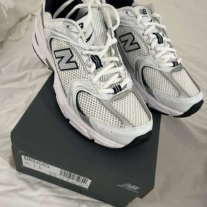 Vita sneakers från New Balance - Snygga vita New Balance sneakers med mörkblå och grå detaljer. Skorna har en ventilerande mesh-ovandel och klassisk snörning. Missade sista returdagen och därför aldrig använda!