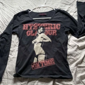 Svart långärmad tröja från Hysteric Glamour - Cool svart långärmad tröja från Hysteric Glamour med tryck av en kvinna och texten 'Hysteric Glamour On Time' i rött och beige. Perfekt för en edgy look.
