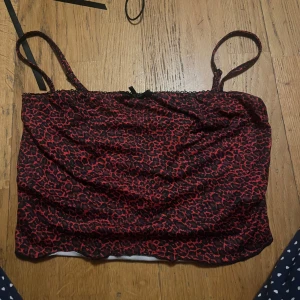 Svart och röd leopardmönstrad tubtopp - Snygg tubtopp med svart och rött leopardmönster. Toppen har smala axelband och en liten rosett framtill. Perfekt för en djärv look!
