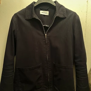 Svart jacka från Weekday - Snygg svart jacka från Weekday med dragkedja framtill och klassisk krage. Perfekt för en stilren look. Jackan har långa ärmar och två praktiska fickor framtill. Skickt 5/10 eftersom jag har klippt insidan pga att det var ett fult material i inne sidan av jackan. Annars funkar den helt normalt 