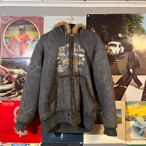 Grå fodrad jacka med foder från HBH Group - Säljer en grå jacka från HBH Group med mjukt foder och huva. Jackan har ett tryck på framsidan och ribbade muddar. Perfekt för kyliga dagar med sin varma insida., fodret på luvan går att ta av.