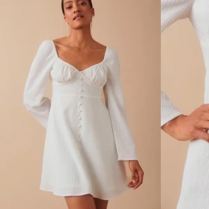 Vit klänning med knappar - Elegant vit klänning med v-ringning och långa ärmar. Klänningen har knappar framtill och passar perfekt inför studenten, aldrig använd och alla lappar kvar!