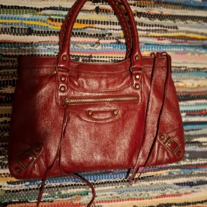 Röd skinnväska med dragkedja - Snygg röd skinnväska med praktisk dragkedja och dekorativa detaljer. Perfekt för att ge din outfit en färgklick. Väskan har både handtag och en avtagbar axelrem för flexibilitet.