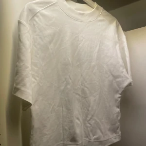 Vit t-shirt från COS - Säljer en stilren vit t-shirt från COS i storlek M. T-shirten har en klassisk design med rund hals och korta ärmar. Perfekt basplagg för alla tillfällen.