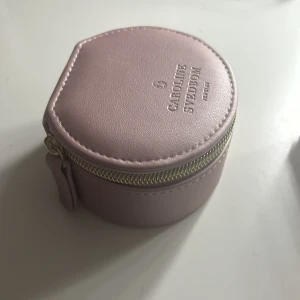 Rosa smyckeskrin Caroline Svedbom - Helt oanvänd ny rosa smyckesskrin från Caroline Svedbom. Perfekt för att förvara smycken säkert. Har en dragkedja och en mjuk insida med en liten påse för extra skydd samt en platta för studs-örhängen.