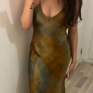 Zara långklänning med smala axelband - Snygg unik långklänning i gröna och bruna toner. Klänningen har smala axelband och en v-ringad halslinje, vilket ger en elegant look. Perfekt för bal eller fest, använd en gång, från zara säljs ej längre! Nypris 1300