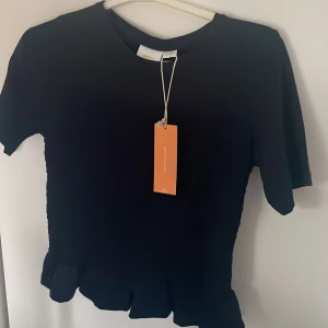 Mörkblå topp med smock - Snygg mörkblå topp från gina tricot med korta ärmar och volangdetalj vid nederkanten. Perfekt för en stilren look. Toppen är i storlek 146/152 men är lagom på mig som är storlek Xs! Köpt för 219