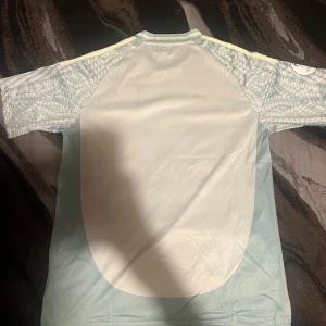 Mexico  fotbollströja från Adidas - Snygg fotbollströja från Adidas med ett unikt mönster i ljusblått och gult. Tröjan har korta ärmar och en rund halsringning. Perfekt för fotbollsfans som vill sticka ut på planen!
