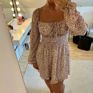 Somrig miniklänning - Superfin blommig miniklänning med långa ärmar och knytning framtill. Storlek 36 men passar även 38. Är 167 cm lång och vanlig S-M. Använd 1 gång.