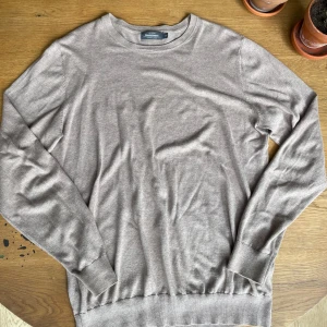 Beige tröja från Dressmann - Säljer en stilren beige tröja från Dressmann i storlek M. Den är gjord av mjuk Supima bomull och har långa ärmar med ribbade muddar. Perfekt för både vardag och lite finare tillfällen. Skön och enkel att matcha med det mesta! Använd vid ett fåtal tillfällen och kvalité skulle jag uppskatta till 9/10!