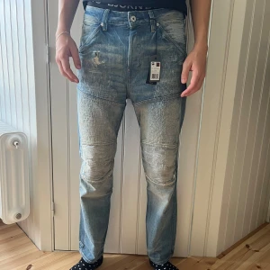 G-Star Raw jeans med slitna detaljer - Säljer ett par snygga G-Star Raw jeans i ljusblå denim. De har en cool, sliten look med flera distinkta slitningar och lappade detaljer. Jeansen har en normal passform och är perfekta för en avslappnad stil. De är helt nya med taggen kvar.