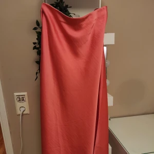 Rosa långklänning från Y.A.S - Säljer en elegant rosa midikjol från Y.A.S. Kjolen är i ett mjukt och glansigt material, perfekt för festliga tillfällen. Den har en stilren design utan ärmar och en vacker drapering. Passar perfekt för alla fester!