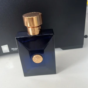 Blå parfymflaska med gulddetaljer - Säljer en elegant parfym i en djupblå flaska med en lyxig guldfärgad kork och en dekorativ guldmedaljong på framsidan. Flaskan har en stilren och modern design som passar perfekt på vilken hylla som helst. Perfekt för den som vill ha en doft med stil och klass. Flaskan har en kod på undersidan: 30116SA.