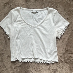 Vit topp - Topp med volanger i sömmarna, kort i modellen, v-ringad och tunnt material 