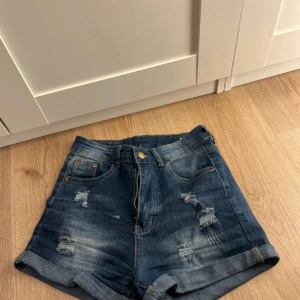 Blå jeansshorts från Shein - Snygga blå jeansshorts från Shein i en avslappnad stil med slitna detaljer. De har en klassisk femficksdesign och en knappgylf. Perfekta för en casual look under varma dagar.
