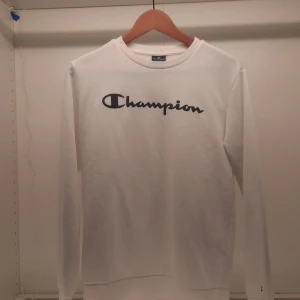 Vit långärmad tröja från Champion - Säljer en stilren vit långärmad tröja från Champion med deras ikoniska logga i svart på bröstet. Perfekt för en avslappnad look. Tröjan är i storlek X-Large och passar bra till både vardag och chill.