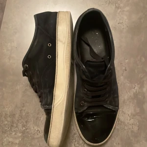Svarta sneakers från Lanvin - Snygga svarta sneakers från Lanvin med en stilren design. Skorna har en blank tå och snörning framtill. Säljs billigt pga skadorna där fram! För fler bilder kom priv🤝