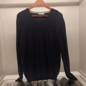 Mörkblå tröja från J.Lindeberg - Säljer en stilren mörkblå tröja från J.Lindeberg med v-ringning. Tröjan har långa ärmar och en diskret logga på bröstet. Perfekt för en klassisk look.