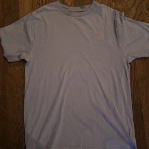 Ljusblå t-shirt från Ralph Lauren   - Säljer en ljusblå t-shirt från Ralph Lauren med en liten broderad logga på bröstet. T-shirten är kortärmad och tillverkad i mjuk bomull. Perfekt för en avslappnad stil.