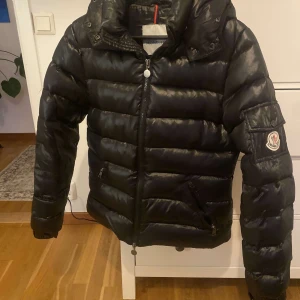 Svart dunjacka från Moncler liknande  - Säljer en snygg svart dunjacka från Moncler liknande med dragkedja och huva. Har ett hål i ena fickan men annars ok skick. 