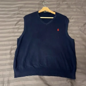 Mörkblå väst från Polo Ralph Lauren - Snygg mörkblå väst från Polo Ralph Lauren med en klassisk v-ringning. Västen har en röd broderad logotyp på bröstet som ger en stilren touch. Perfekt för lager-på-lager under kyligare dagar. Ord pris 2000! Pris kan diskuteras!
